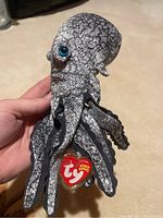 Hand holding the Opie Beanie Baby plush showing detailed front side with blue eyes and Ty heart tag