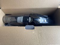 Handheld vacuum cleaner in open cardboard box showing product inside.