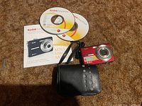 Kodak EasyShare M763 digital camera with case, user manual and software discs displayed on a brown carpet.