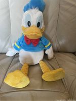 Donald Duck plush in sitting position on a beige couch showing front view and detailed character features.