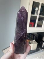 Front view of the polished purple fluorite crystal tower held in hand showing pointed tip and veining.