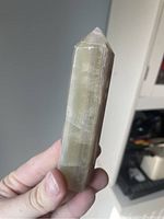 Fluorite crystal tower showing green and yellow bands, held in hand against blurred background