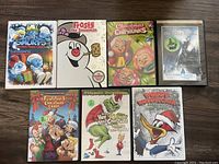 Seven kids Christmas-themed DVDs arranged on a wooden surface showing the front covers.