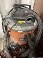 Ridgid shop vacuum cleaner orange and black with attached hose and power cord on top, needs cleaning.
