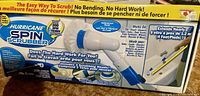 Box showing packaging of Hurricane Spin Scrubber with product details including waterproof feature, 300 RPM spin speed, and compatibility with various surfaces like tile, grout, tubs, patios, and more. The box also highlights the inclusion of three scrubbing heads and an extendable pole up to 4 feet.
