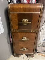 Front view of the vintage wooden cabinet showing three drawers with decorative wood panels and brass handles.