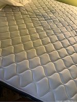 Close up of full size mattress top surface showing quilted wave pattern fabric in light color.