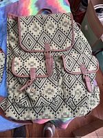 Front view of canvas backpack with black geometric tribal pattern, brown trim, and multiple flap pockets