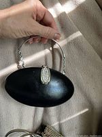 Black Daniella hand clutch held in hand showing metal handle and clasp detail