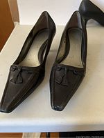 Pair of black leather pumps with tassel detail, pointed toe, showing wear and creases on surface, labeled Bandolino.