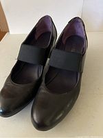 Black leather Mary Jane shoe with stretch band and visible wear on toe and sides, size 7.5
