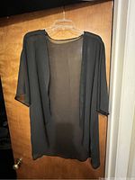 Black sheer cardigan hanging on a hanger in front of a wooden door.