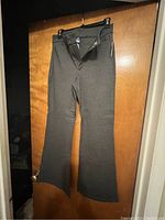 Grey flared trousers hanging on a door, showing full length and flare style