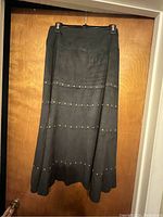 Full view of the Athena Marie dark grey skirt hanging, showing ankle length and placement of decorative metallic tacks in horizontal rows.