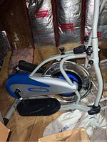 Side view showing the foot pedal, flywheel, and lower frame structure of the elliptical machine.