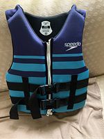 Front view of navy blue Speedo youth flotation vest with teal stripes, zipper and buckle straps.