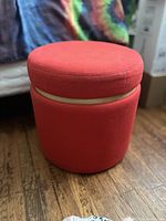 Side view of red round ottoman storage stool showing cylindrical shape and removable lid in red fabric.