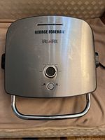 Top view of George Foreman Grill & Broil showing stainless steel top with dials and logo.