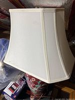 Close-up view of the white fabric lamp shade with visible dirt and marks, the red floral lamp base partially visible underneath.