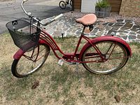 Side view of vintage red bicycle with black metal front basket, tan spring saddle, and rear fender.