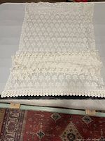 View of white lace curtain panel showing intricate Victorian lace pattern with scalloped edge and hanging loops.