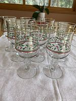 Front view of 8 Arby's Christmas-themed stemmed glasses arranged in two rows on a white cloth with a window background