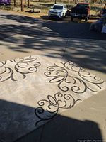 Photo showing white area rug with black swirls laid on driveway with shadow cast, highlighting pattern and condition.