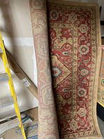 Partial rolled-up view showing the rug's inner rolled design and the outer decorative floral border in red, beige and cream tones.
