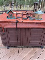 Full view showing one birdhouse style feeder, two flower pot holders, tall tube feeder with black leaf cage, and shepherd's hook leaning against hot tub cover.