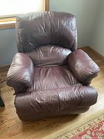 Front view of a large burgundy leather recliner showing padded back and armrests with visible creases.