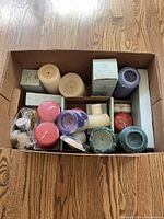 Top view of a cardboard box containing a variety of pillar and tea candles in different colors and packaging, some labeled Party Lite.