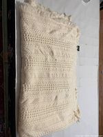 Photo showing the full folded wool blanket with fringe edges and cable knit pattern texture.