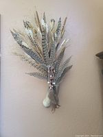 Close-up photo of Native American themed wall hanging showing feather arrangement, dried plants, and bead/shell accents.