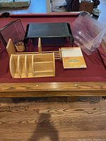 Photo of clear plastic file organizer, wooden desk organizers including letter holder and compartment tray, black metal mesh organizer, and small wicker pen holder displayed on a pool table.
