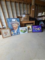 Five framed pictures and posters displayed on the floor in a storage space with natural wood beams in the ceiling.