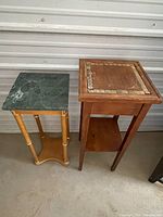 Photo showing two plant stands side by side, one with a green marble square top and wooden legs, the other with a wood top featuring decorative inlay and detailed edges.