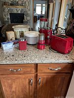 Kitchen countertop view showing all small appliances and kitchen tools arranged including blender, slow cooker, toaster, coffee grinder, salad spinner, and boxed appliances on granite counter.