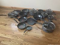T-Fal cookware set arranged on wooden floor showing variety of pots, pans, lids.