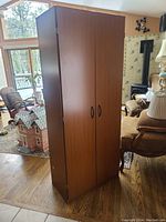 View of the closed two door storage cabinet showing wood-grain finish and handles.