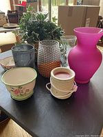 Photo showing various vases in different materials and colors along with an artificial ivy plant on a table