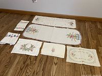 Full layout of all nine vintage embroidered linens including pillowcases, dresser scarves, and dollies arranged flat on wooden floor.