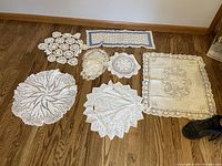 Overview of eight vintage tatting linen pieces in various shapes and sizes on hardwood floor