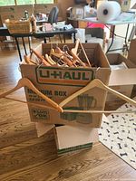 Box packed with over 50 wooden clothes hangers of different types, including standard and pants hangers, showing light natural wood finish.