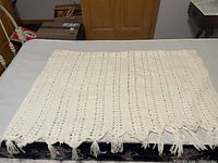 Full view of the cream wool knit blanket spread out, showing its knit pattern and fringed edge.