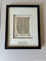 Full view of framed original page mounted in black shadowbox frame with white mat and descriptive caption below.