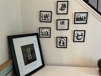 Eight framed black and white silhouette artworks on a wall and one additional piece leaning on a table corner. Each artwork depicts a scene from Hans Christian Andersen fairytales.