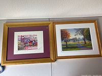 Photo of two framed limited edition prints side by side. Left print is a colorful small San Francisco scene matted in burgundy with a wooden frame. Right print is a golf course scene in a gold frame.