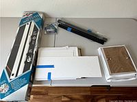 Top view showing the large Logan Compact Mat Cutter Model 30 in its box, cut mats, and magnetic poster hangers on the table