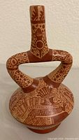 Front view of Peruvian stirrup spout vessel showing detailed painted patterns on handle and body.