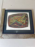 Framed colorful abstract serigraph with geometric shapes and four perforations, shown with ruler for scale.